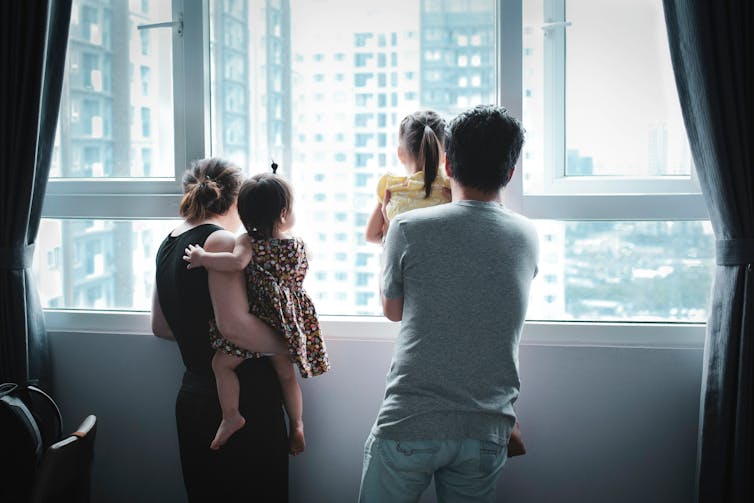 Mehe ja naise seljaosa, kes mõlemad hoiavad last, vaadates aknast välja kõrghoonete hoonetes.
