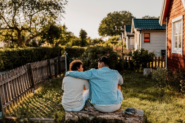 Tagumine vaade noormehele, kellel on käega meessoost sõbra ümber, istub päikesepaistelisel päeval tagahoovis