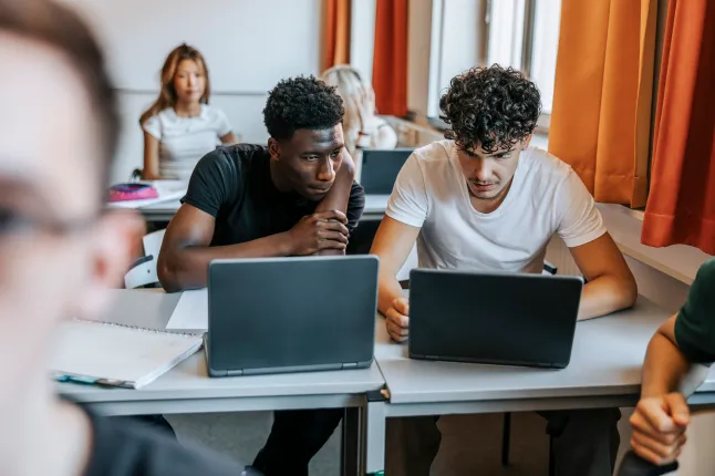 Mitmerassilised meessoost keskkooliõpilased arutavad klassiruumis sülearvuti taga