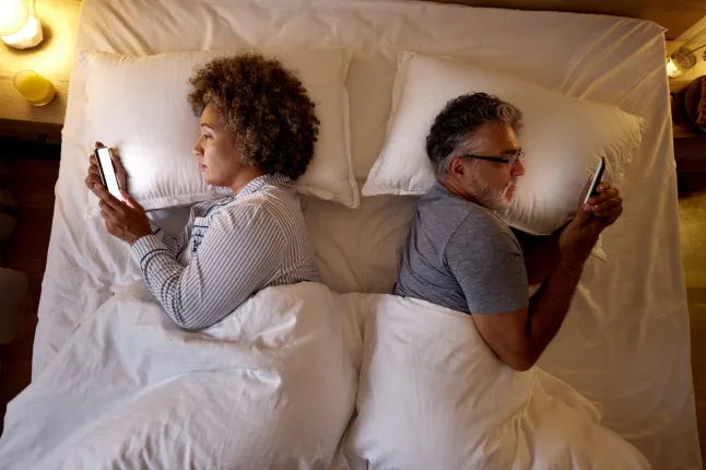 Ülaltoodud vaade lõdvestunud küpsest paarist, kes kasutab voodis mobiiltelefone.