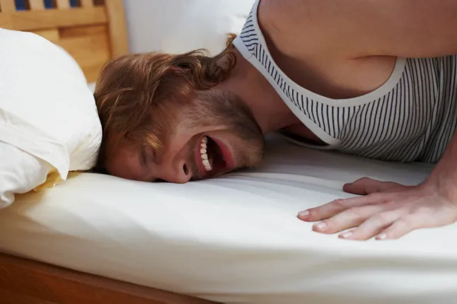 Poolpikk intiimne kaader atraktiivsest mehest, kes naerab ja lükkab pead voodisse