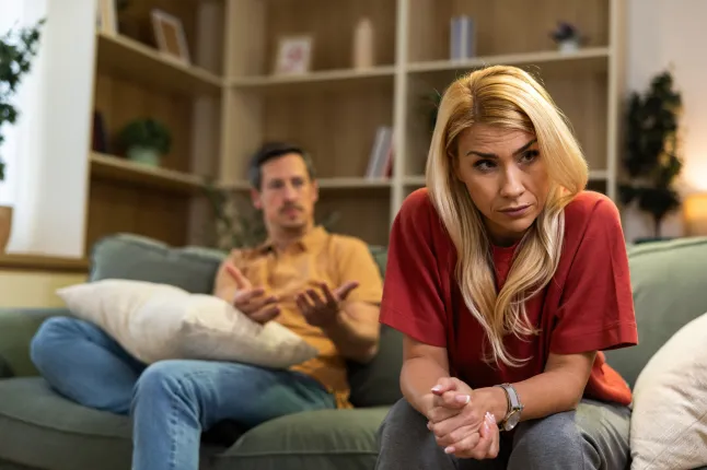 Paar istub diivanil koos ühe inimesega, kes näeb kodus ärritunud, samal ajal kui teised liigutavad kodus vestluse ajal