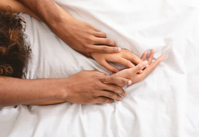 Mees ja naine hoiavad voodis seksimise ajal käest kinni.