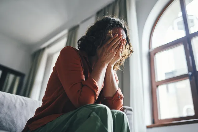 Stressis naine, kes istub toas ja katab kätega nägu