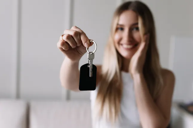 Särava naeratusega rõõmus noor naine hoiab käes võtmekomplekti, kui ta kohtub oma uue korteri sissepääsu juures kinnisvaramaakleriga.