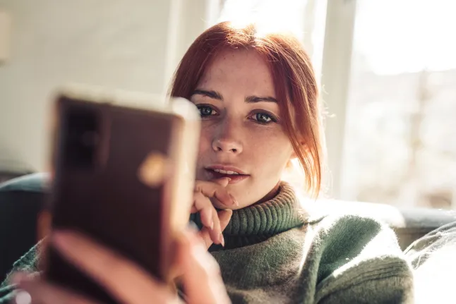 Punaste juustega naine vaatab oma mobiiltelefoni ekraanilt.
